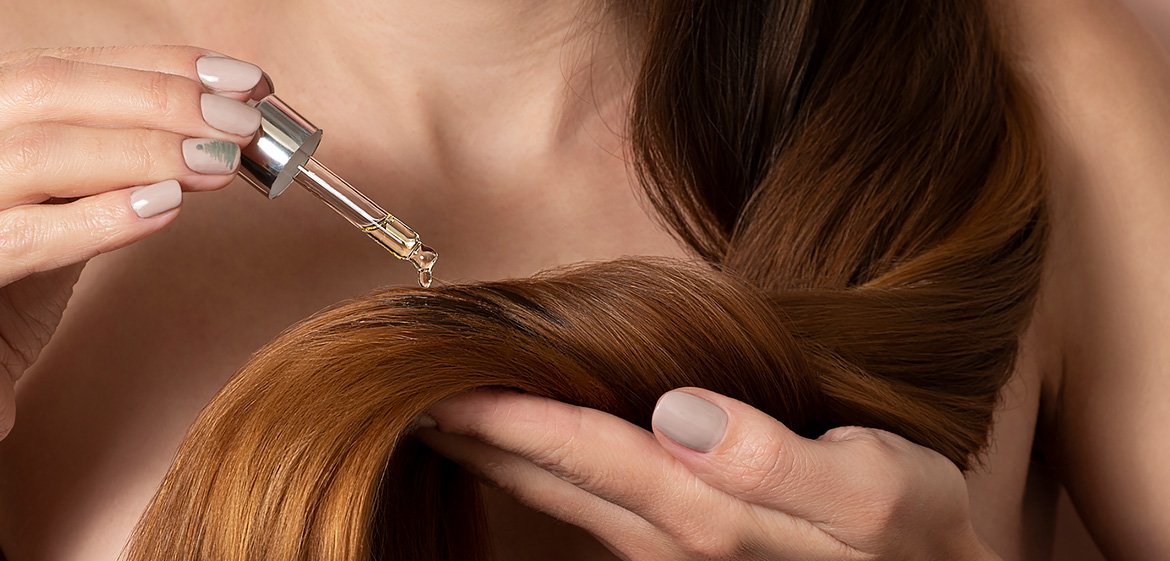 Close-up auf braunes Haar auf das behutsam ein Serum aufgetragen wird.